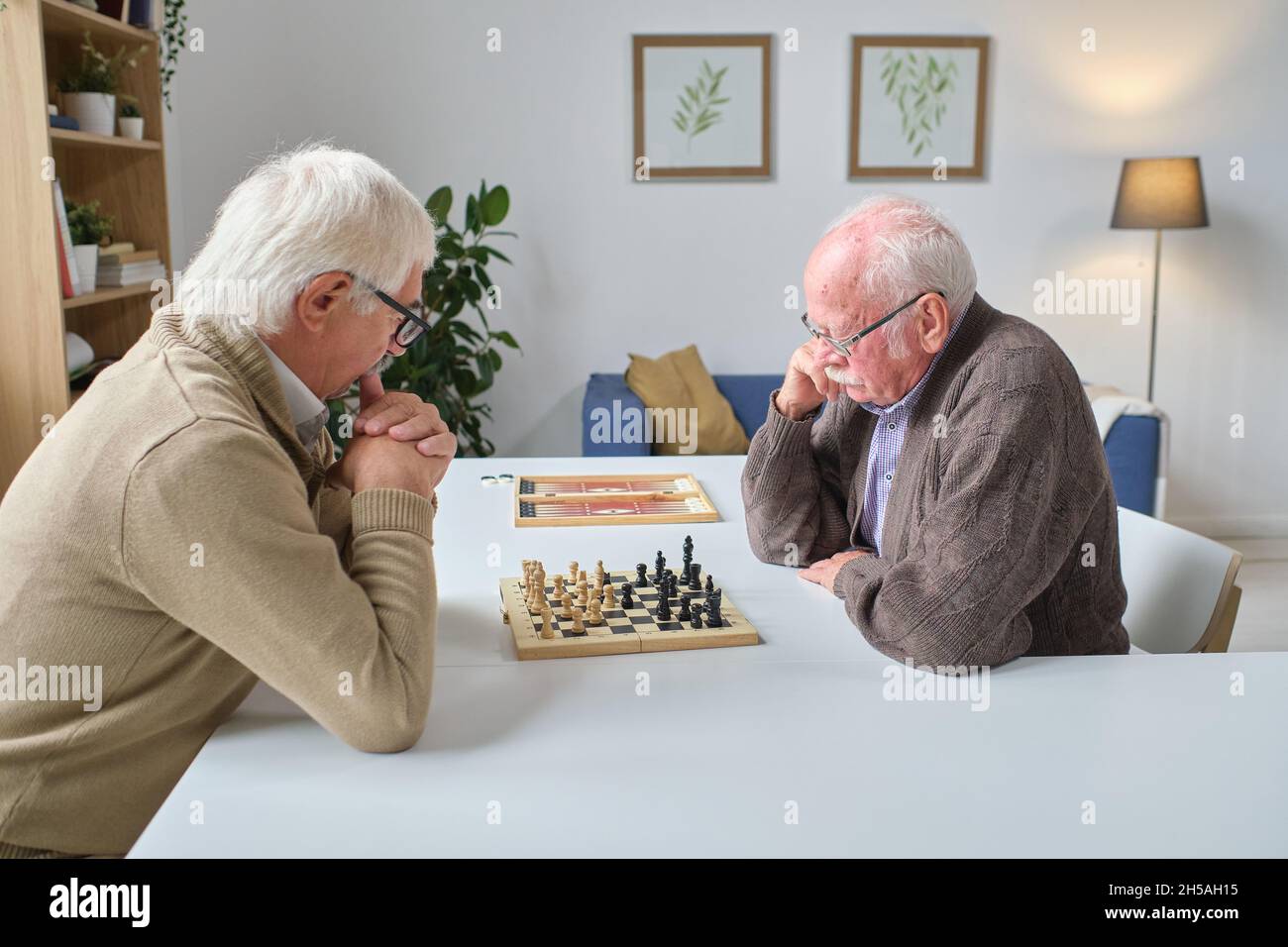 Due uomini anziani seduti al tavolo e che giocano a scacchi nella stanza Foto Stock