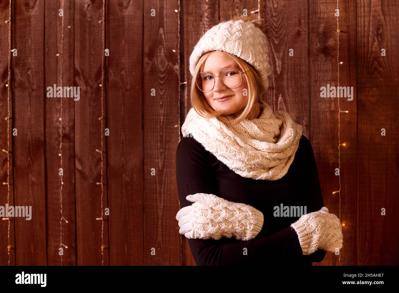 Ritratto bella ragazza con capelli corti in cappello a maglia e guanti caldi su sfondo di legno Foto Stock