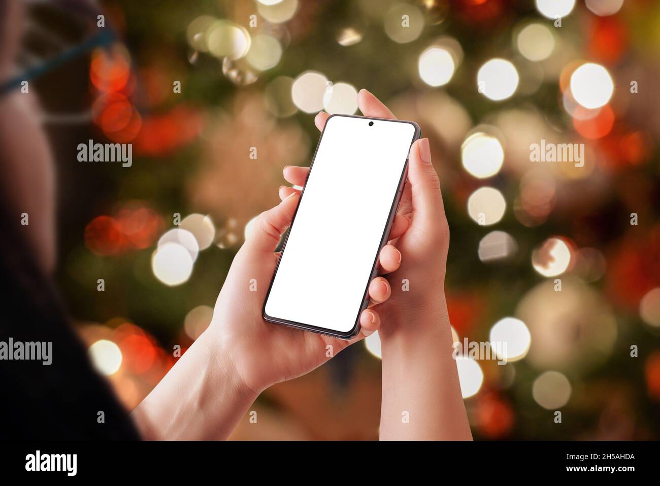 Telefono mockup in mani donna con un sacco di luci di Natale in background. Display isolato con smartphone integrato Foto Stock