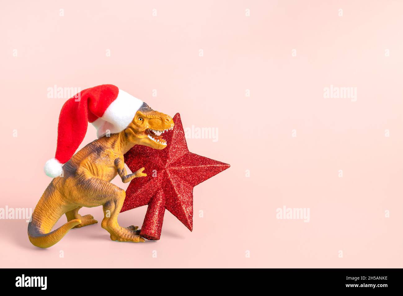 Il Rex del dinosauro in cappello rosso di Babbo Natale tiene la stella nelle relative zampe su sfondo rosa la vigilia di Capodanno o la vigilia di Natale scheda di festa d'arte creativa idea per Merry Foto Stock