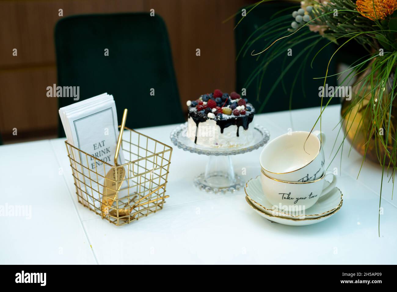 Una squisita torta alla bacca su un supporto di vetro su un tavolo con un vaso di fiori e un set da tè in un moderno design interno. Messa a fuoco selettiva morbida, art nois Foto Stock