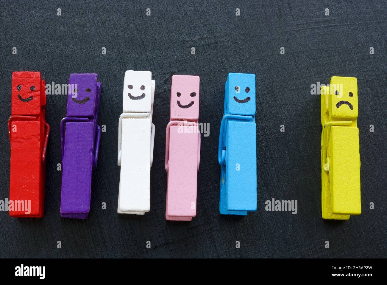 Clothespins con i volti felici e quelli infelici. Concetto di bullismo e inclusione. Foto Stock Clothespins con i volti felici e quelli infelici. Concetto di bullismo e inclusione. Foto Stock
