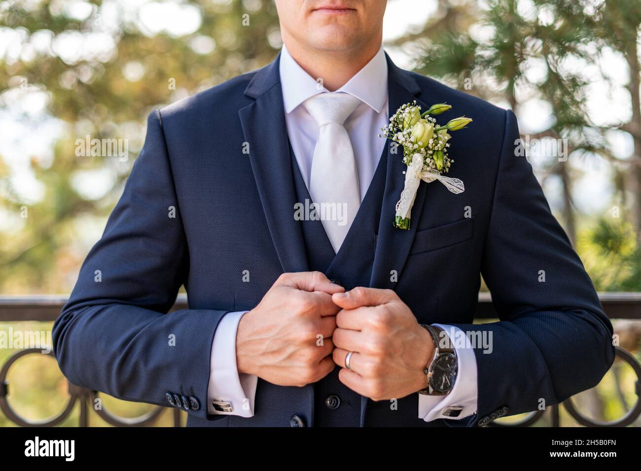 Irriconoscibile giovane sposo in elegante abito blu scuro con belle rose  bianche boutonniere. Dettaglio moda per lo sposo Foto stock - Alamy
