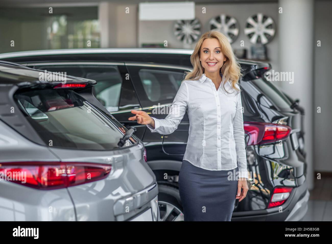 Donna sorridente con un gesto invitante presso la concessionaria auto Foto Stock