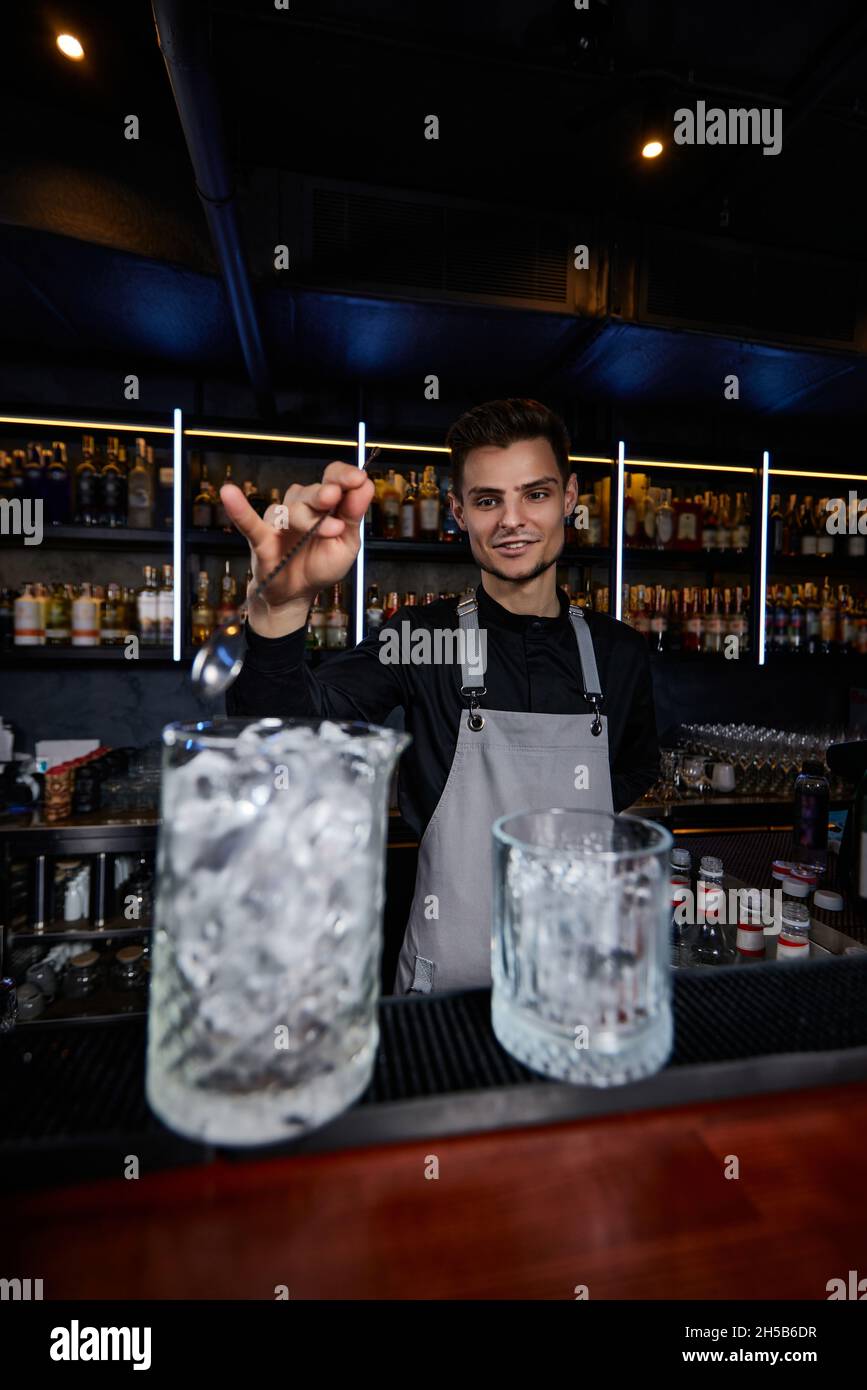 Barman mescolando cubetti di ghiaccio in bicchiere da cocktail con cucchiaio Foto Stock