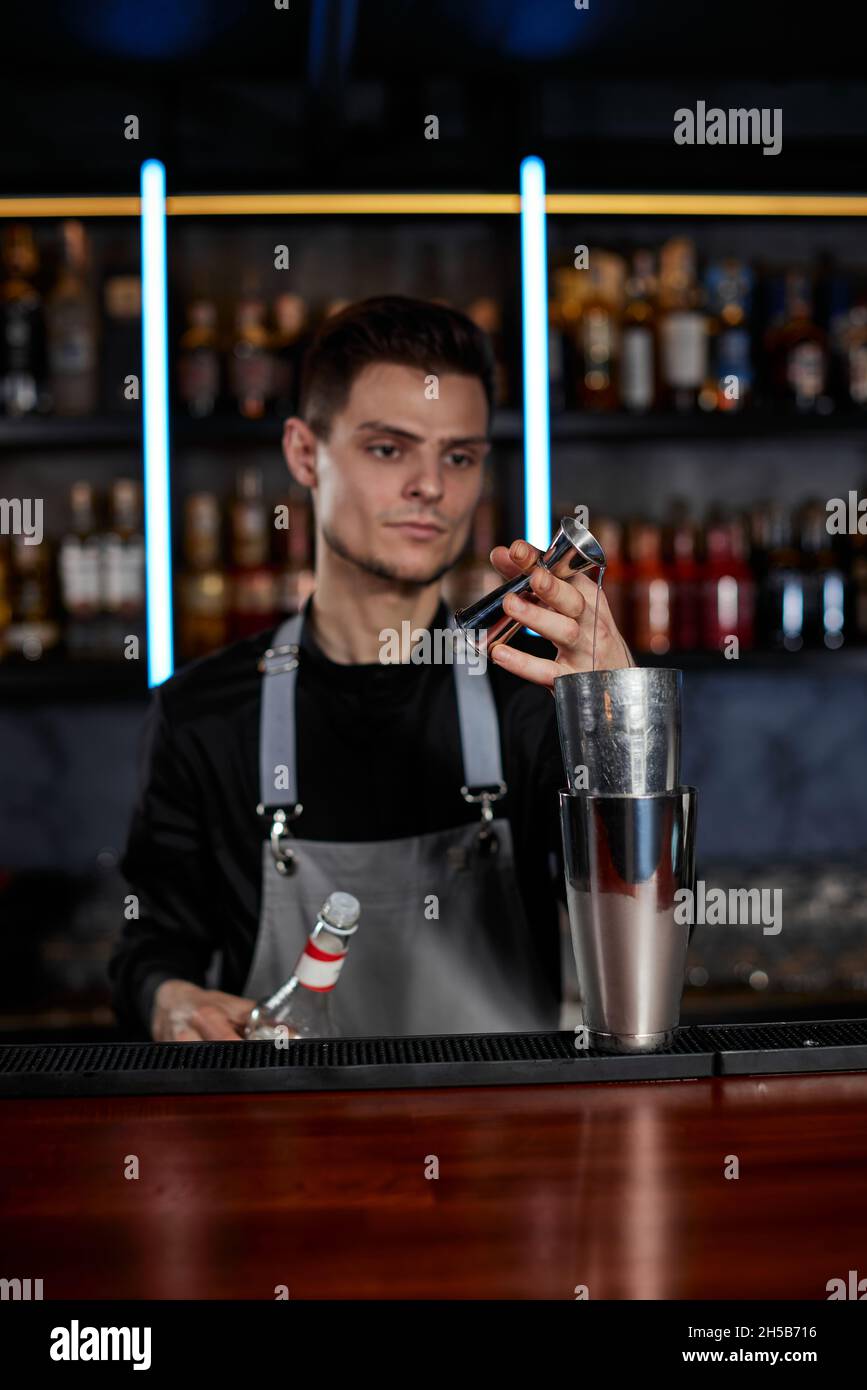 Il barista in grembiule aggiunge l'ingrediente allo shaker Foto Stock