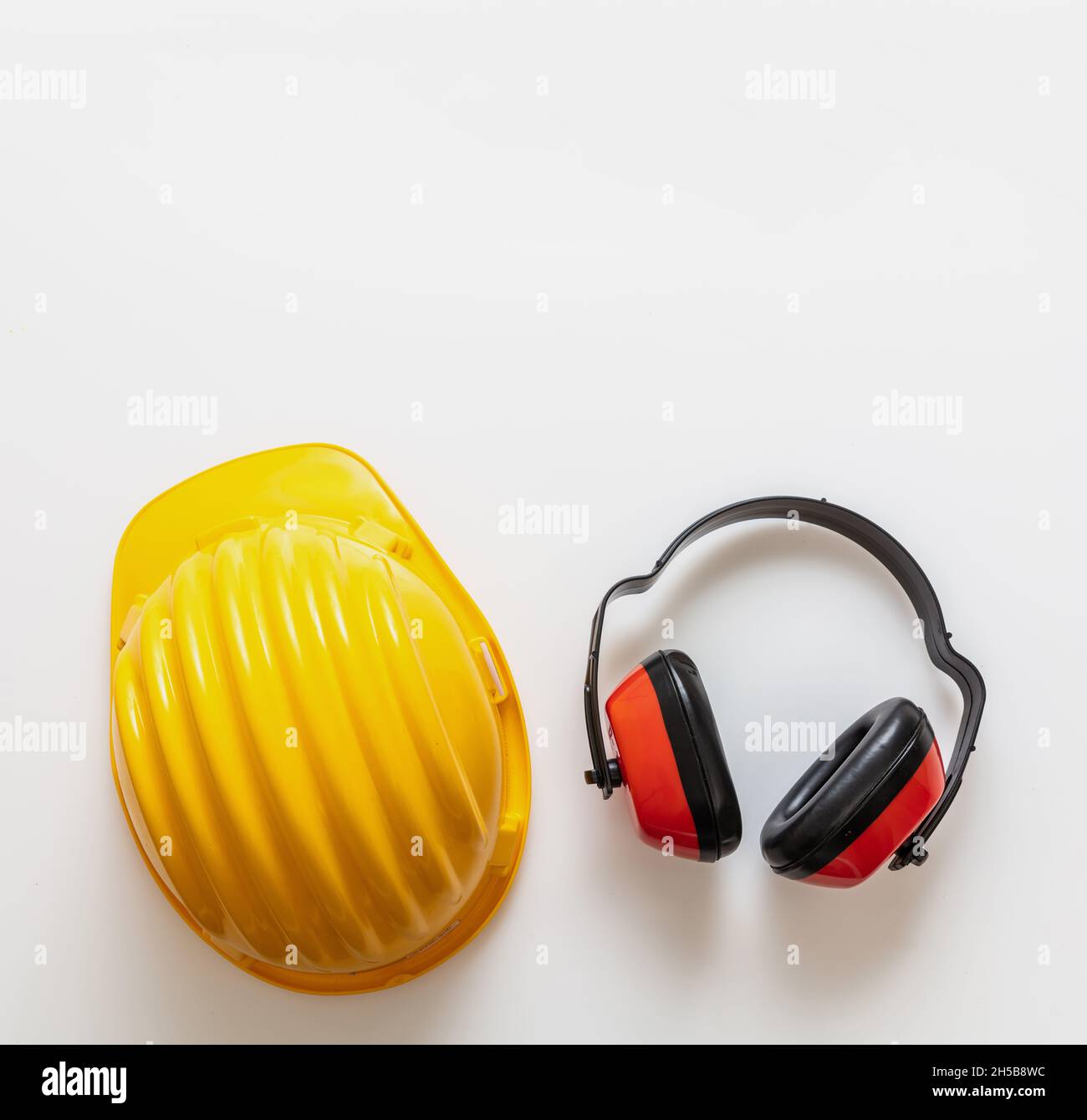 Equipaggiamento di sicurezza casco e cuffie isolate su sfondo bianco, vista dall'alto. Protezione per la testa e l'udito, protezione personale per la testa, giallo rigido Foto Stock