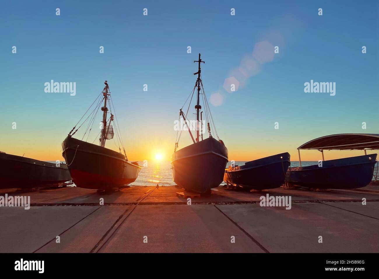 Diverse barche da pesca con alberi sono tirate verso la riva durante il tramonto sul mare Foto Stock