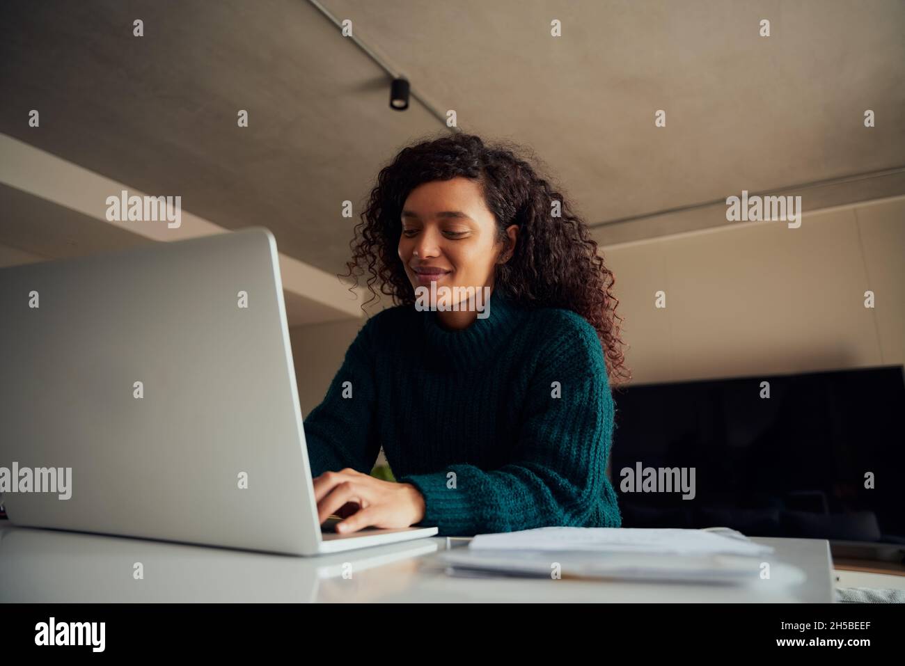 Donna multiculturale adulta seduta al bancone, digitando sul laptop sorridendo Foto Stock