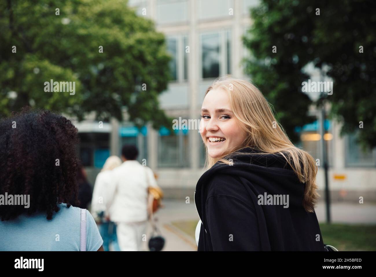 Ragazza sorridente che guarda sopra la spalla mentre cammina con gli amici Foto Stock