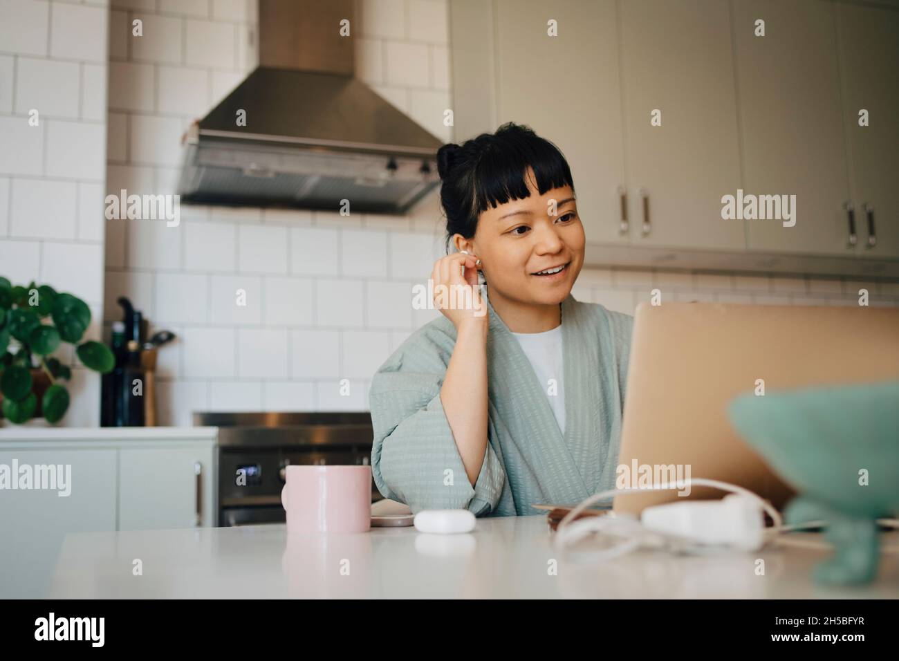 Donna sorridente che parla con una videochiamata attraverso un computer portatile in cucina domestica Foto Stock