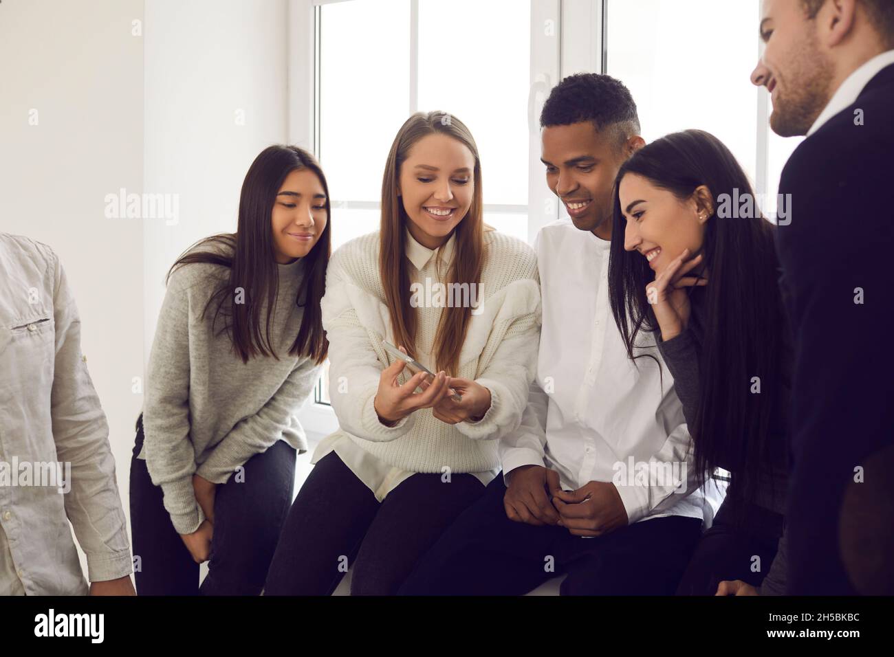 Ragazza allegra che mostra ai suoi amici un divertente meme o una foto sul suo smartphone Foto Stock