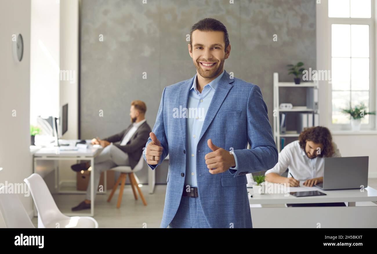 Un dipendente o un leader aziendale felice in carica, sorridendo e dando i pollici in su Foto Stock