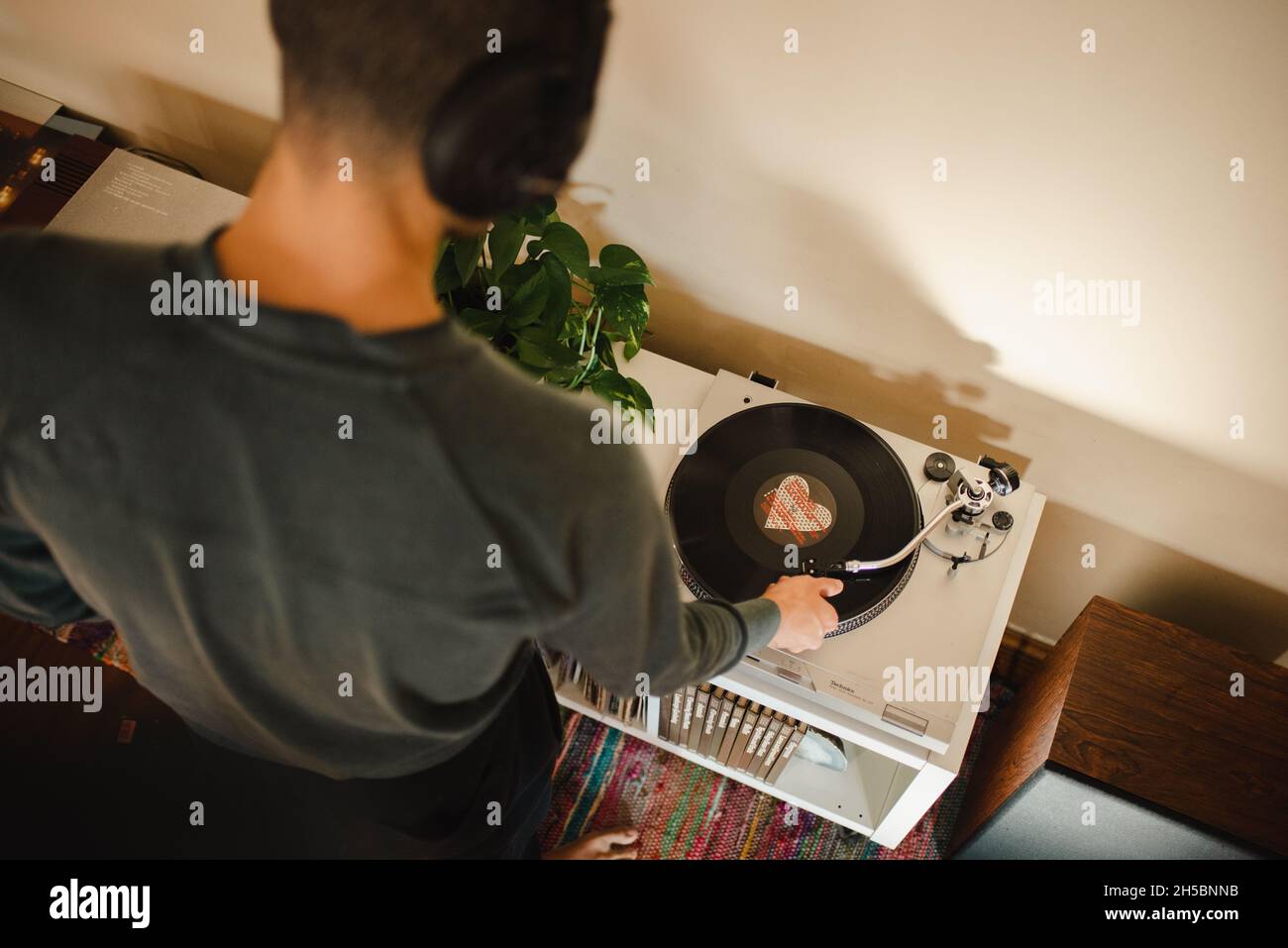 Il giovane uomo millenario della corsa mista mette Needle sul disco in vinile, ascoltando la musica con le cuffie sul suo appartamento. Vista aerea delascolto di musica Foto Stock