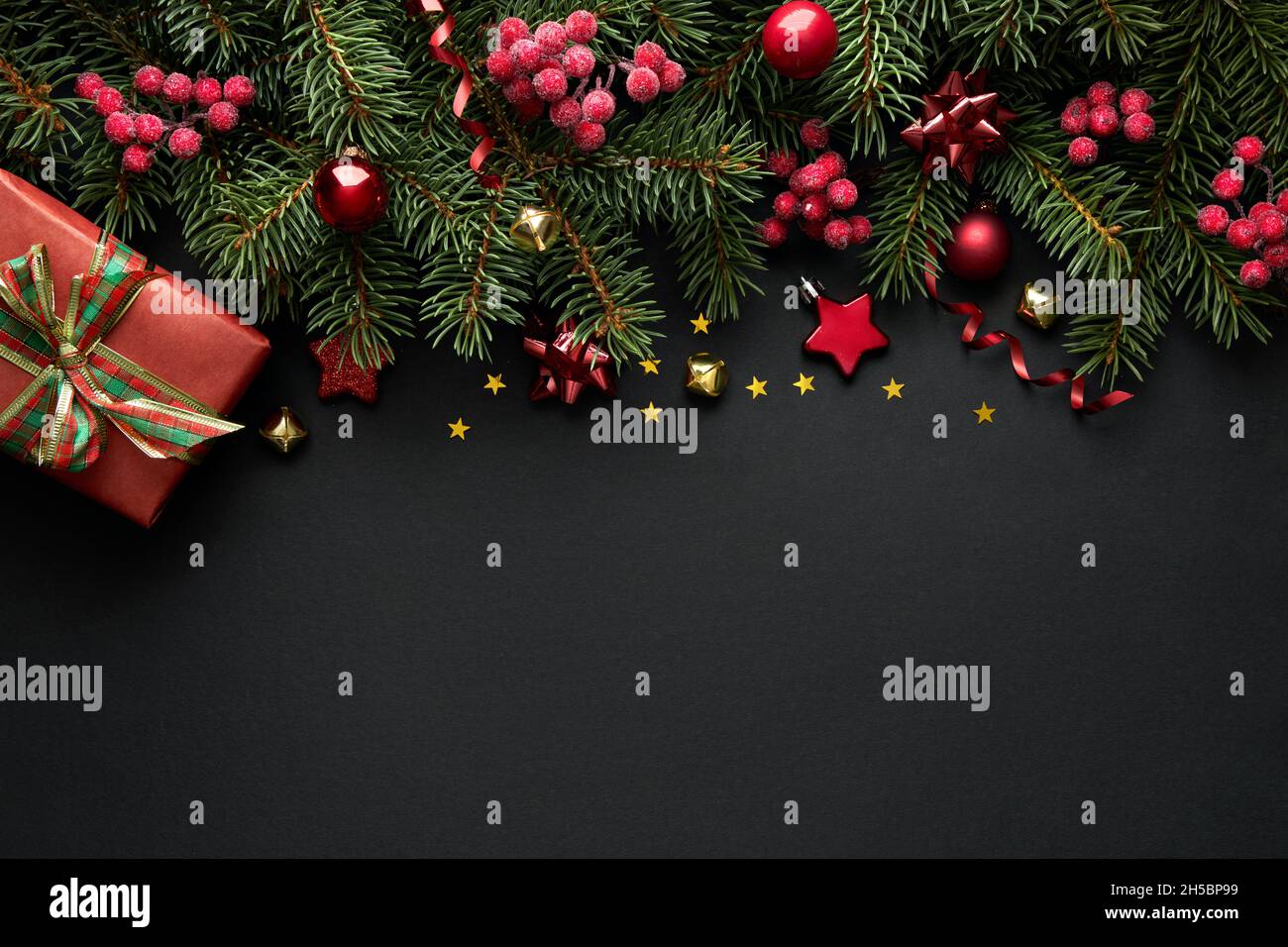 Sfondo natalizio nero con rami di albero di Natale e bacche rosse, composizione natalizia invernale con spazio copia. Vista dall'alto. Foto Stock