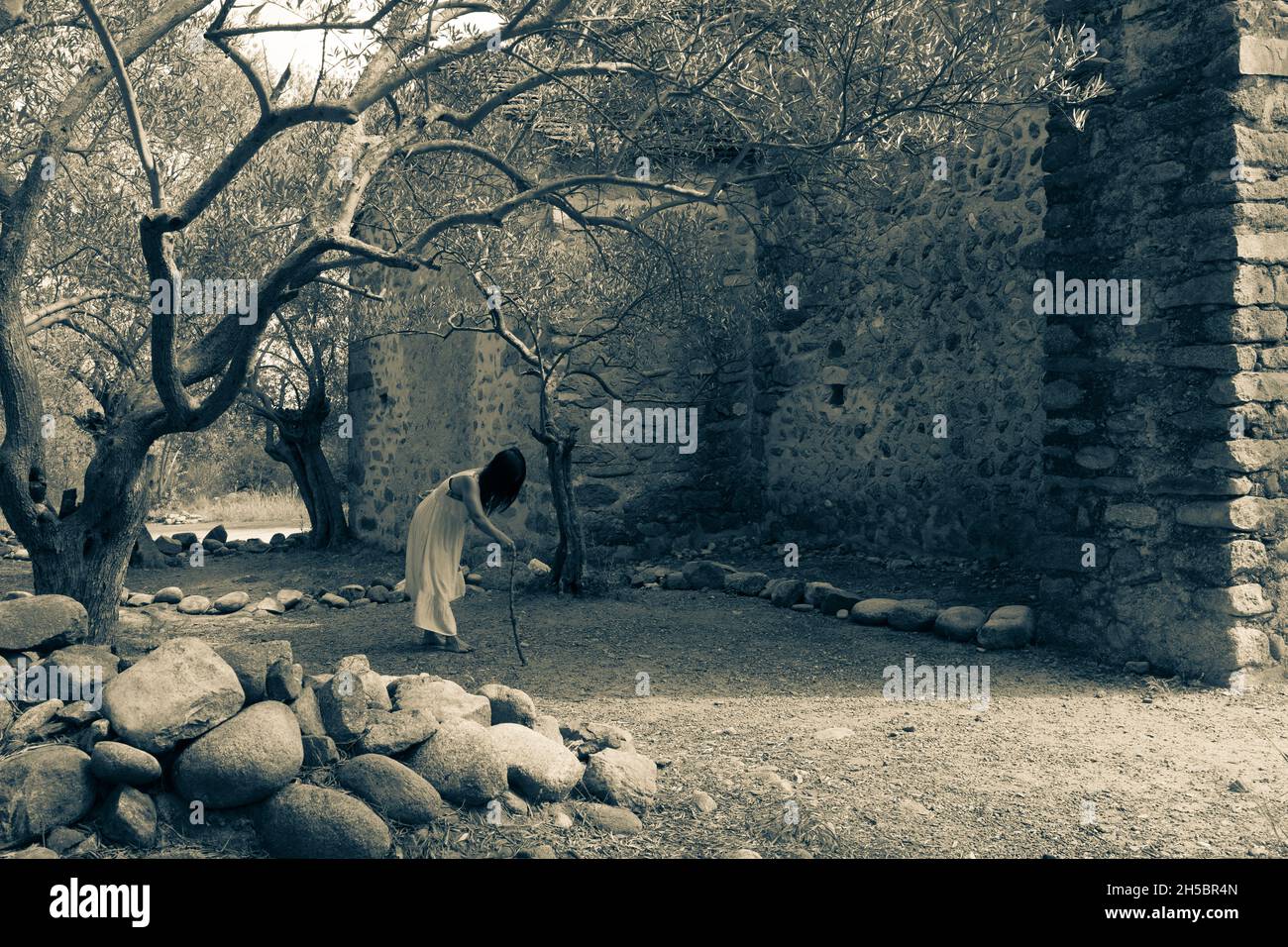 Donna asiatica senza volto fantasma che cammina in una piantagione di uliveti contorta abbandonata vicino ad una vecchia cappella cristiana. Foto Stock
