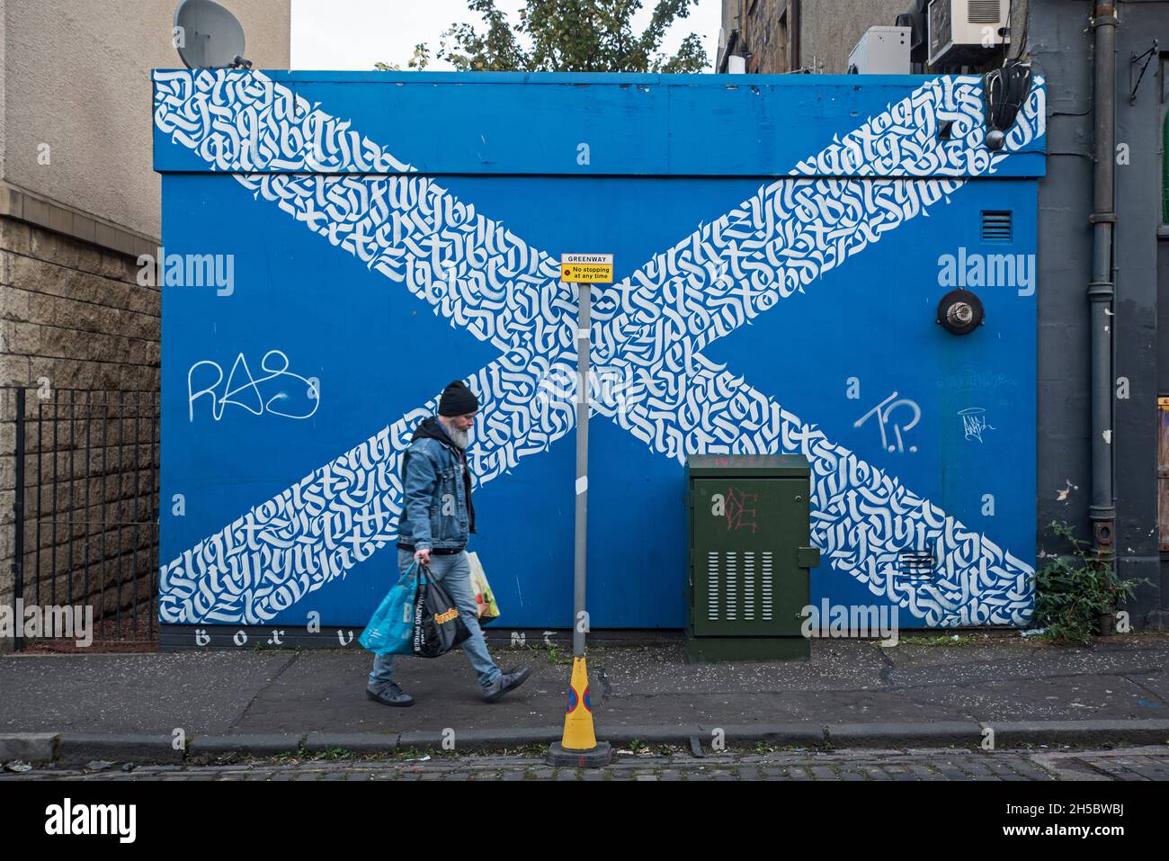 Uomo con le borse portaerei di shopping passeggiando lungo la strada di Sestyre Scozzese a Leith, Edimburgo, Scozia, Regno Unito. Foto Stock
