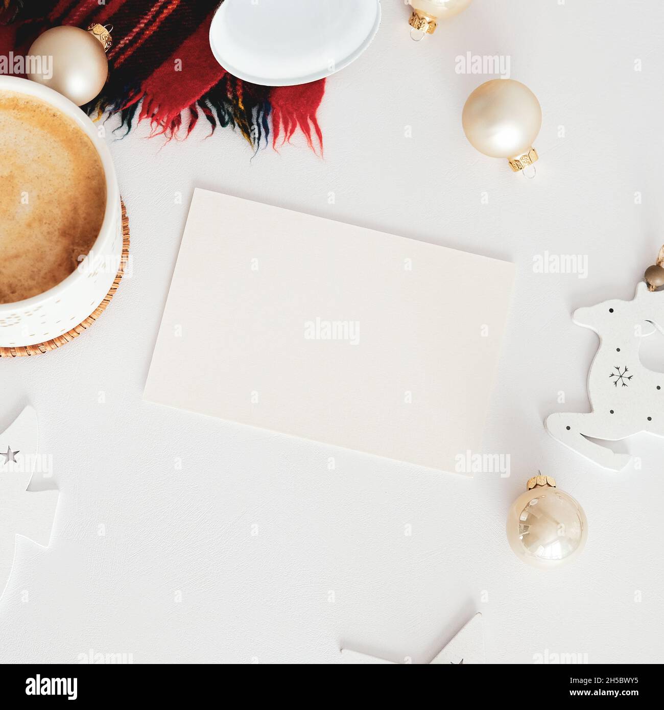 Disegno della scheda di Natale. Mockup carta bianca, tazza di caffè, palline beige, sciarpa, campana su tavola bianca. Disposizione piatta, vista dall'alto, spazio di copia Foto Stock