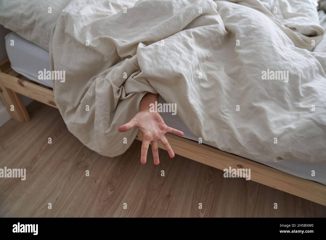 Primo piano della mano di un bambino, sdraiato a letto la mattina, la mano che sporge da sotto la coperta. Foto di alta qualità Foto Stock