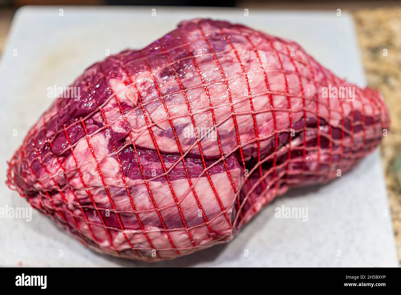 Carne di agnello cruda rossa neozelandese o australiana a parte intera con imballaggio a rete sul tagliere per la preparazione della cottura Foto Stock