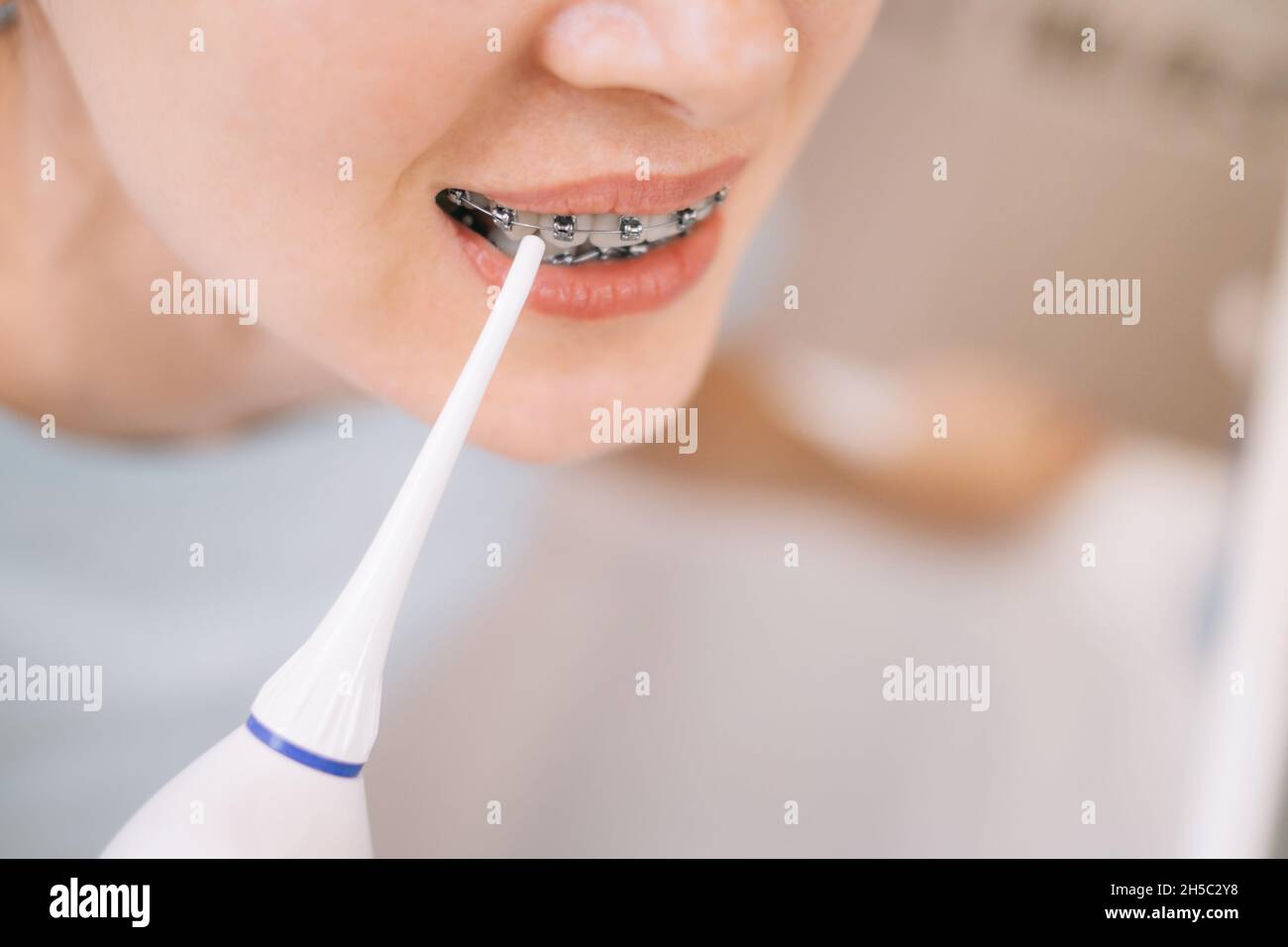 Donna irriconoscibile con bretelle sui denti che gli spazzolano i denti con usando un irrigato, primo piano, prima dello specchio. Foto Stock
