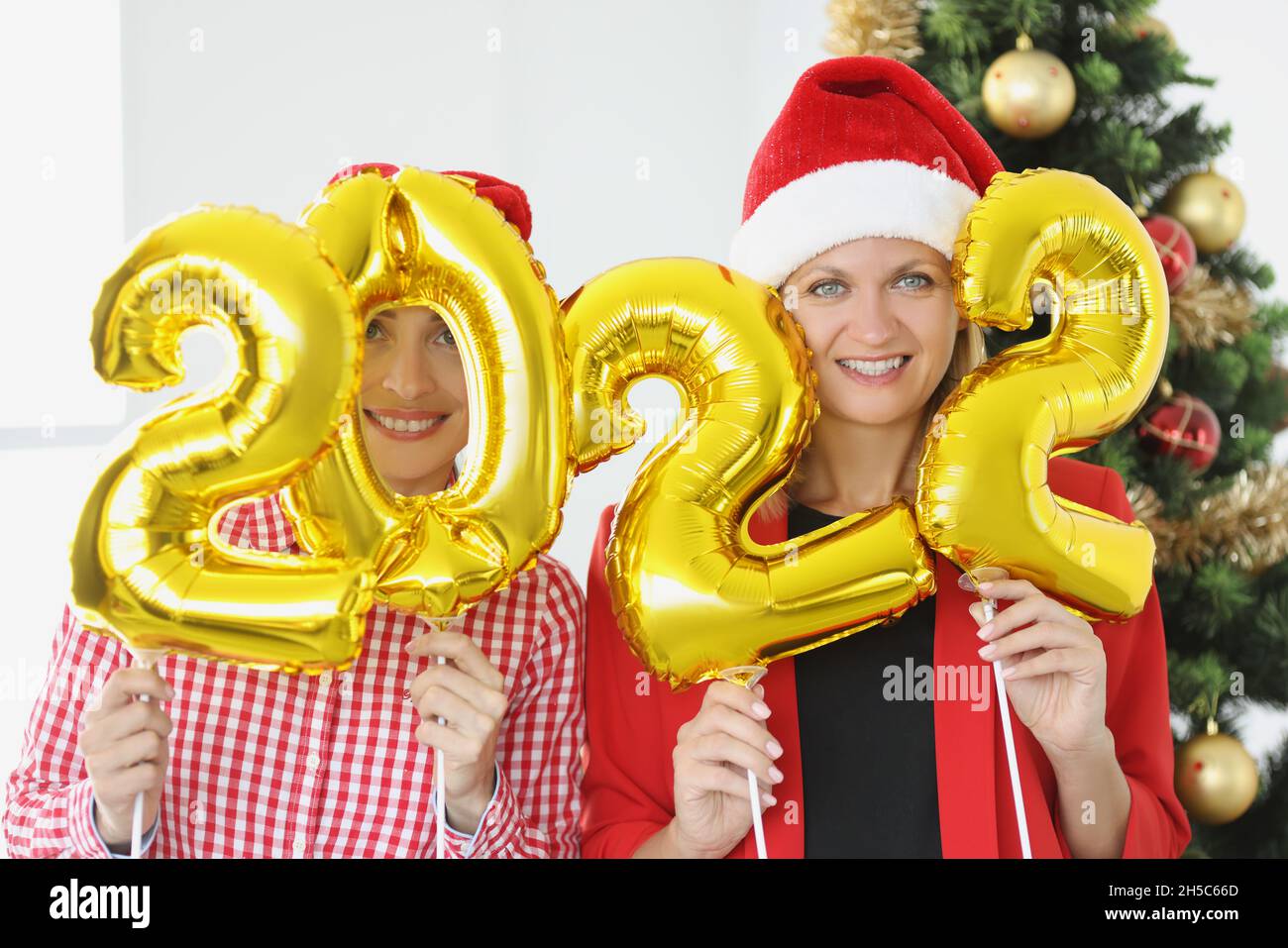 Ritratto di due giovani donne che detengono numeri 2022 in mani contro di albero di Capodanno Foto Stock