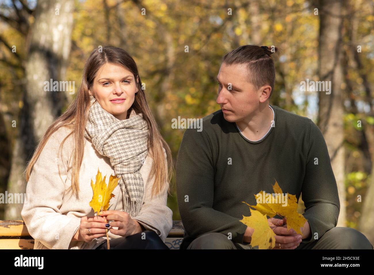 Rapporto, famiglia, concetto di stagioni. Splendida e felice giovane coppia seduta su panchina nel parco durante l'autunno soleggiato e caldo giorno in alberi con giallo Foto Stock