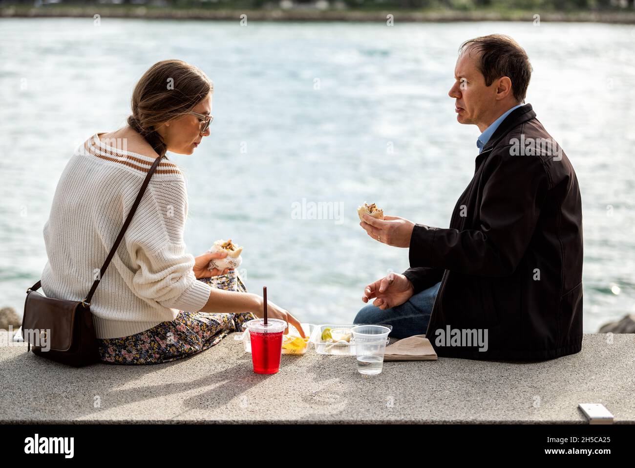 Miami Beach, USA - 17 gennaio 2021: Parco South Pointe con due candidi persone sedute a Bay Water a Miami, Florida, che mangiano sandwich e cibo per il pranzo Foto Stock