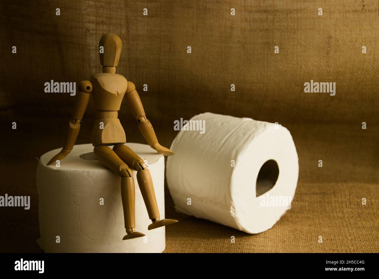 Immagine di un manichino di legno manichino che è seduto su un rotolo di carta igienica accanto ad un altro rotolo con lato chiaro e sfondo marrone scuro con copia spac Foto Stock