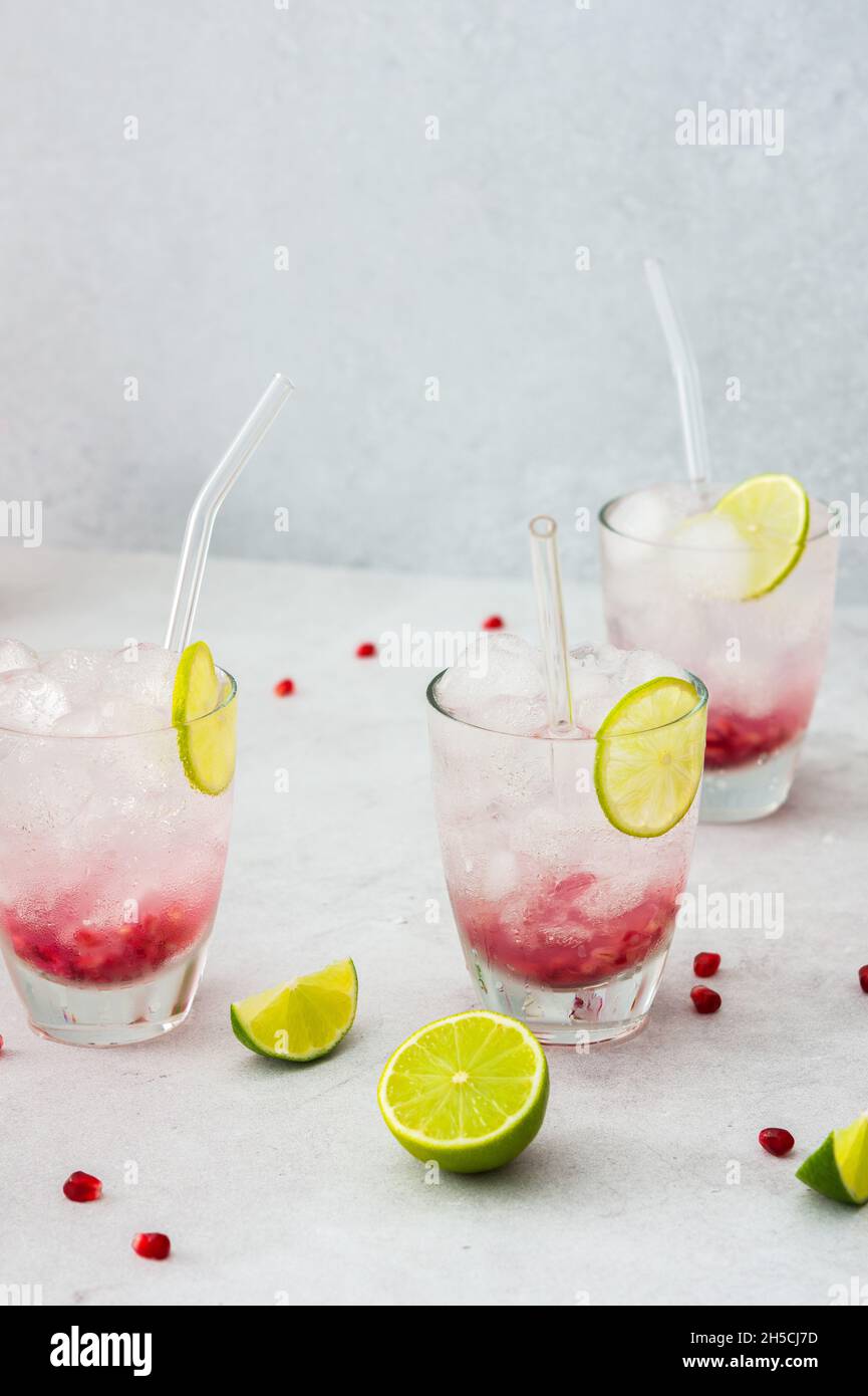 Rinfrescante bevanda di melograno in bicchieri con semi di melograno e cannucce di ghiaccio, lime e vetro Foto Stock