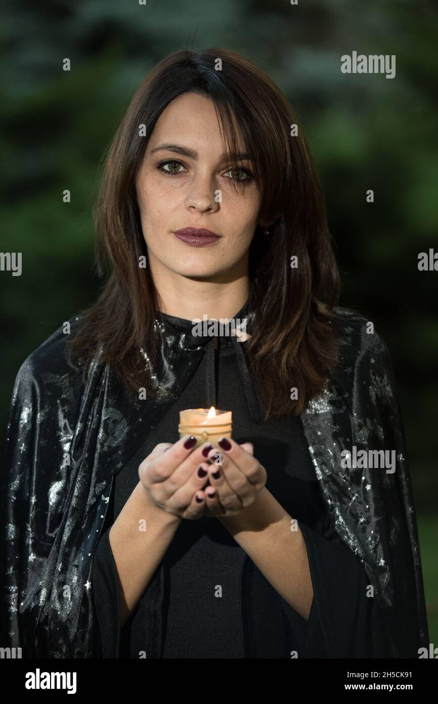 Ritratto di una giovane donna attraente in un abito nero con un mantello. Nelle mani di una candela che brucia. Una ragazza con capelli scuri e occhi verdi marroni e m Foto Stock