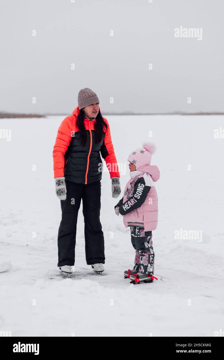 Passeggiata invernale nella natura. Giovane donna e bambina pattinare sul fiume ghiacciato, mamma e figlia Foto Stock