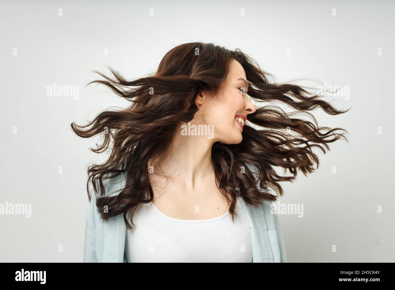 Ritratto di una bella bruna allegra con capelli ricci scorrevoli, sorridente, ridente, su sfondo bianco. Foto Stock