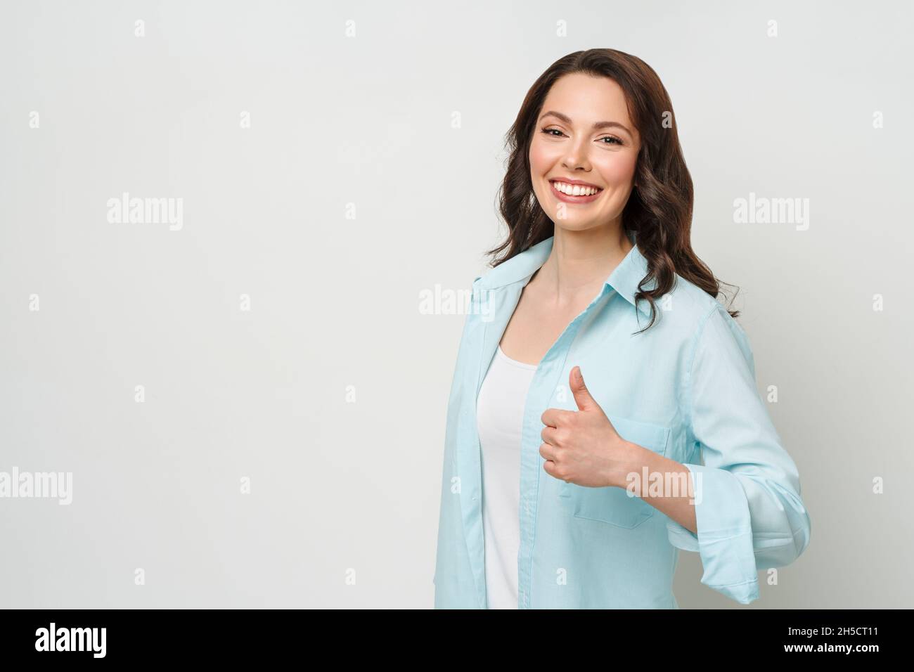 Entusiasta motivata attraente giovane donna , bruna, dando un pollice su gesto di approvazione e di successo con un sorriso raggiante. Foto Stock