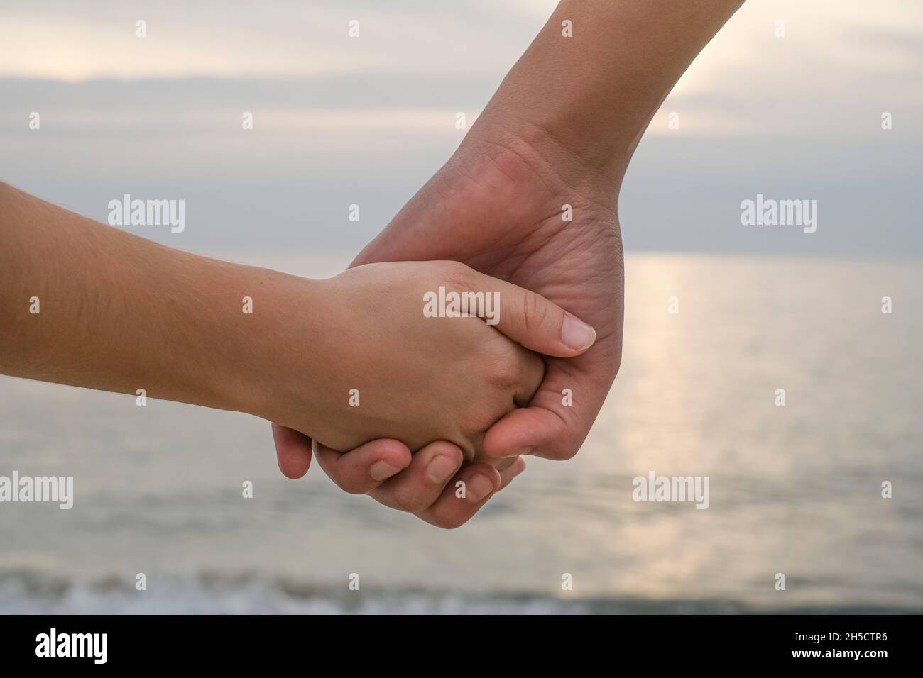 Mamma e figlio capretto mani sopra tramonto mare sfondo, famiglia amore relazione Foto Stock