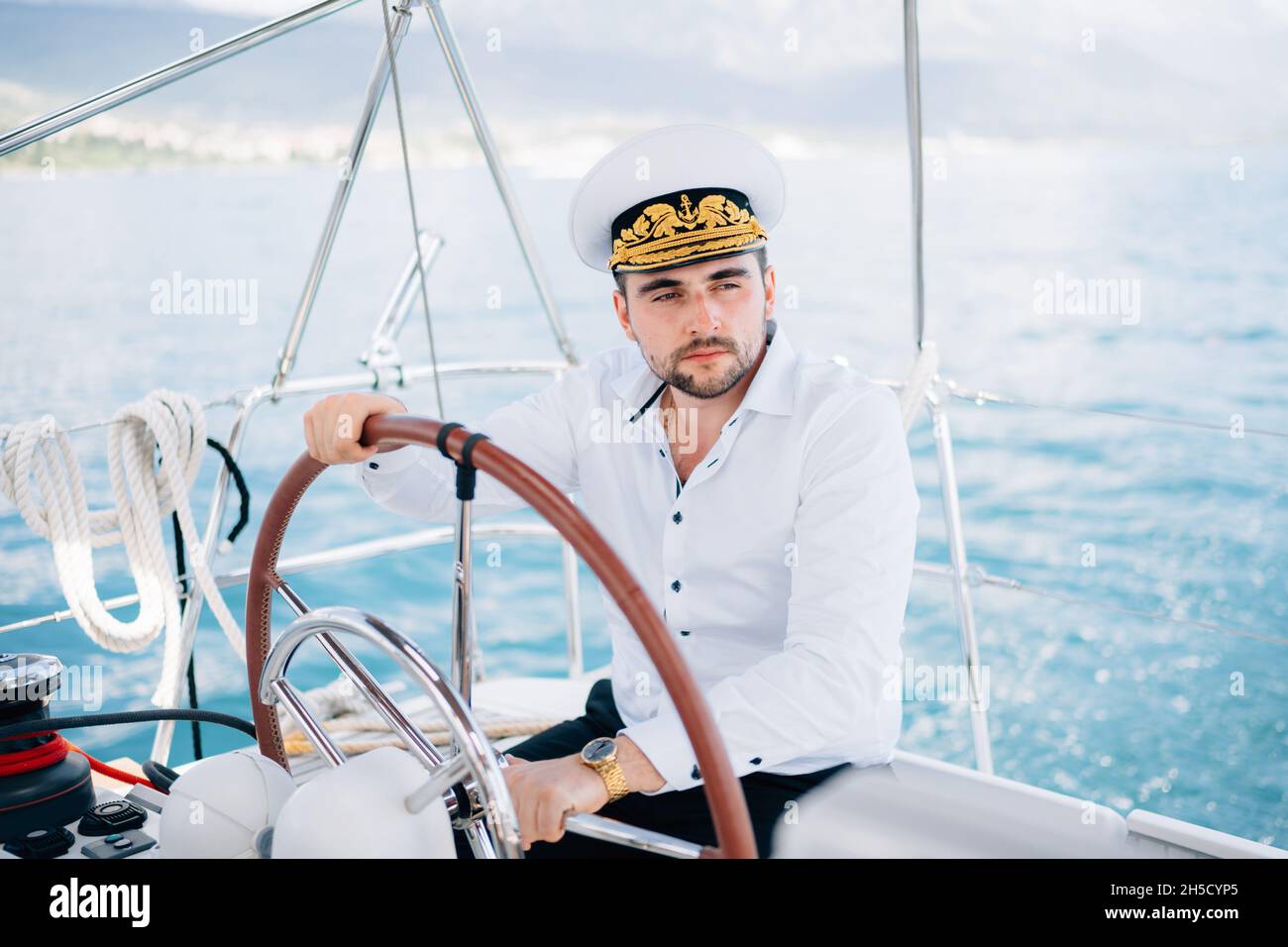 Un uomo in berretto di un capitano siede al timone su uno yacht che naviga  in mezzo al mare Foto stock - Alamy