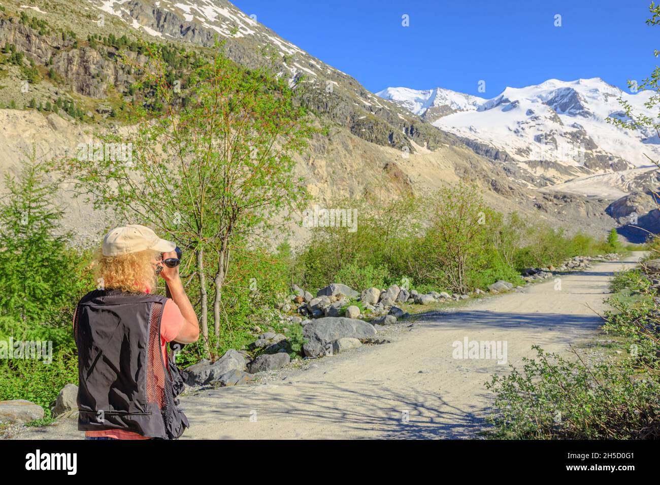 Fotografo uomo con una macchina fotografica che riprende il ghiacciaio Morteratsch sul sentiero in Svizzera. Il più grande ghiacciaio della catena Bernina delle Alpi di Bundner in Foto Stock
