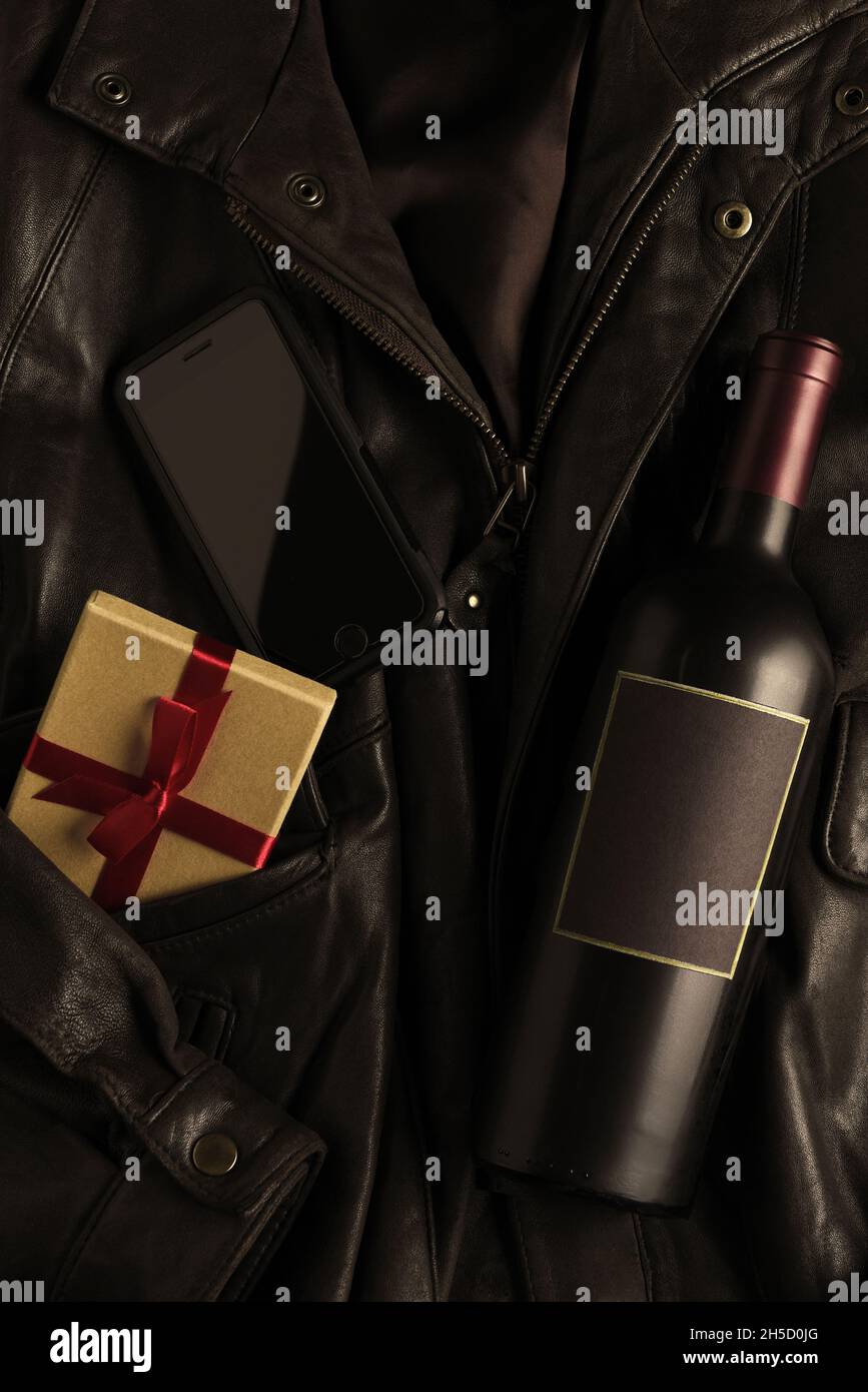 Bottiglia di vino, regalo e cellulare su un bomber in pelle. Disposizione piatta con spazio di copia. Foto Stock