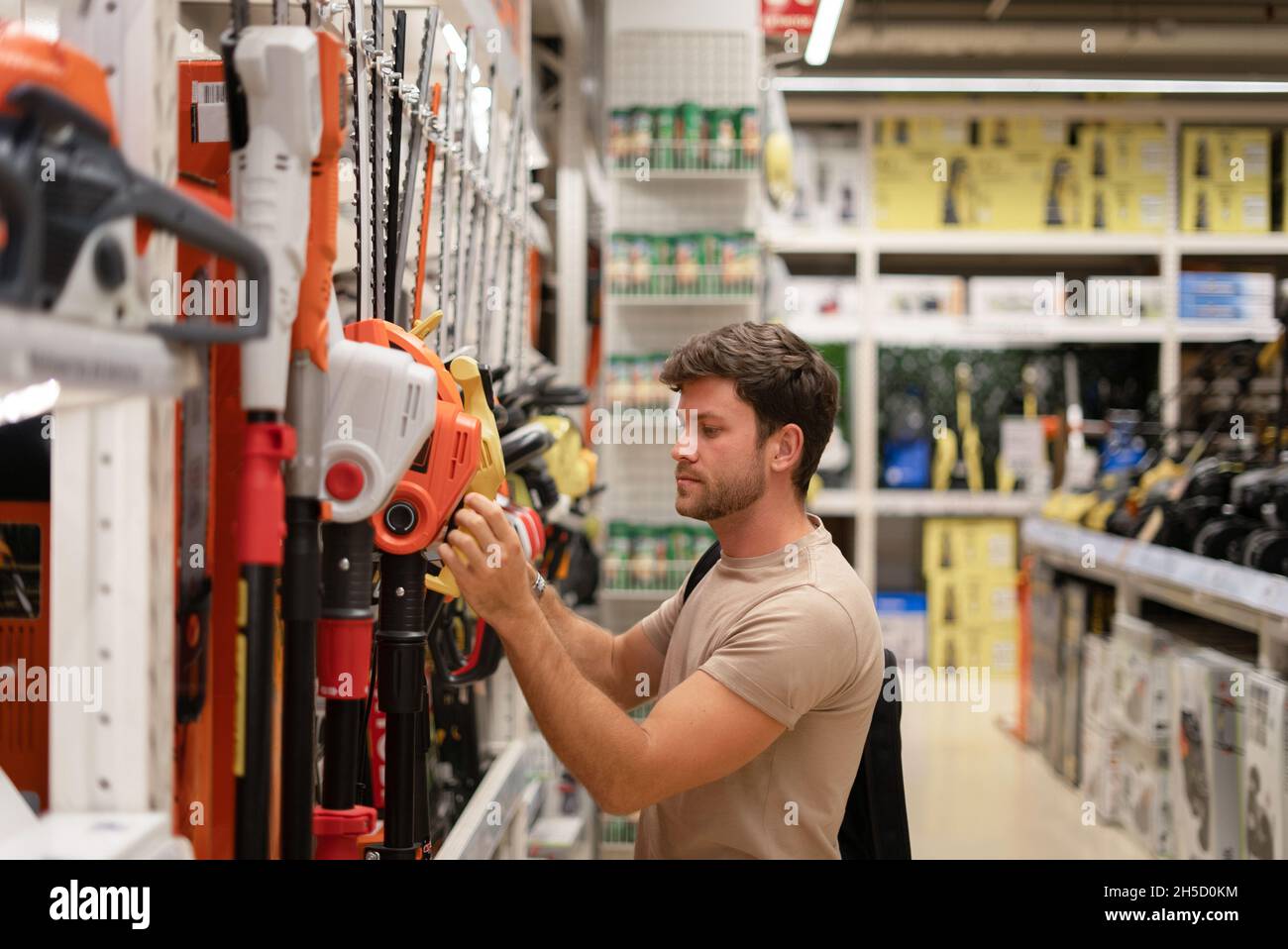 Vista laterale del bel ragazzo casual shopping nel negozio di utensili elettrici e la raccolta di nuovo tagliasiepi Foto Stock