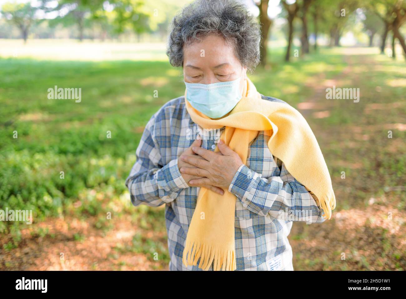 Donna anziana che indossa la maschera medica e si aggrappa al petto nel dolore Foto Stock