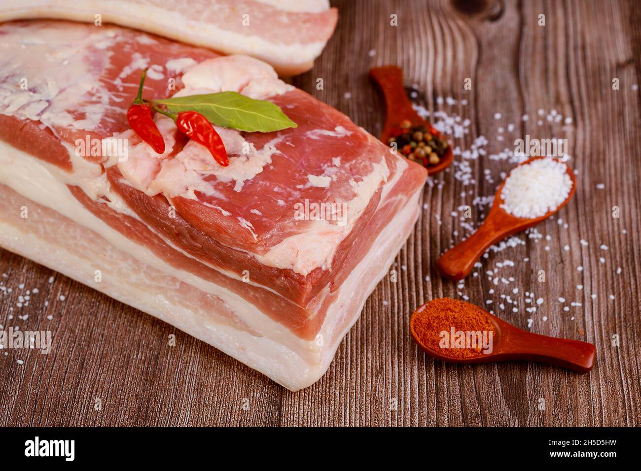Un pezzo di pancia di maiale con spezie su sfondo di legno. Foto Stock