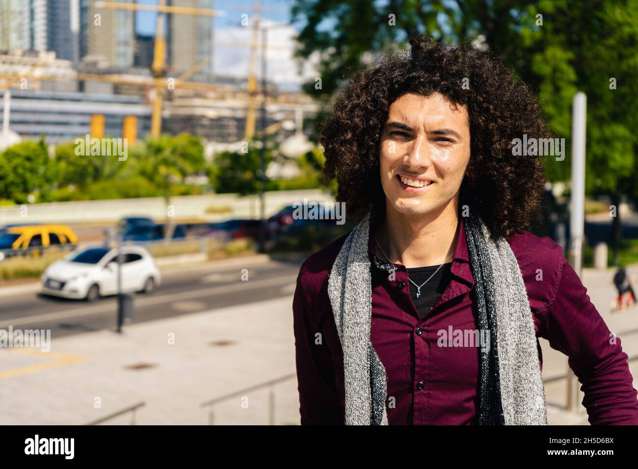 un ritratto di un giovane latino sorridente riccio che indossa una maglietta per strada. Foto Stock