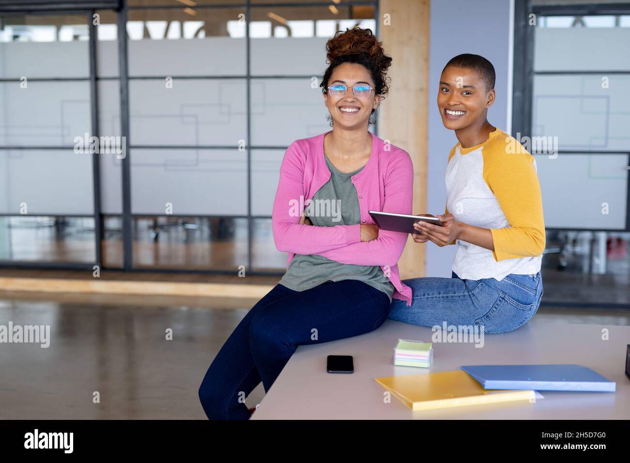 Ritratto di sorridenti donne d'affari multirazziali in casuals seduti sulla scrivania in ufficio creativo Foto Stock