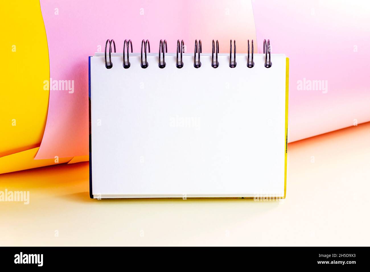 Bianco copybook da ufficio vuoto con spirale mock up per note e messaggi su sfondo luminoso e colorato. Modello di pagina del blocco note vuoto con spazio di copia Foto Stock