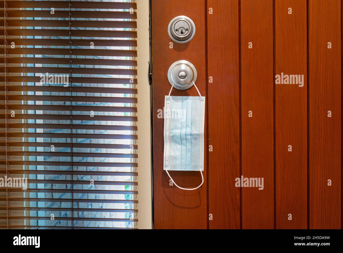 Una maschera medica è appesa al pomello della porta come un prompt di portare un segno quando si lascia la casa durante la pandemia di Covid-19. Foto Stock