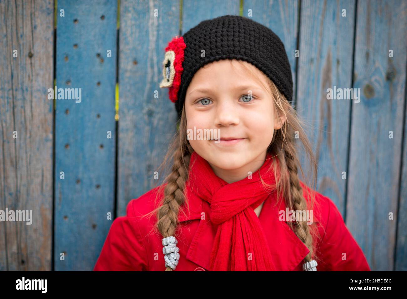 ritratto di ragazza sorridente in impermeabile rosso e sciarpa vicino recinzione di legno Foto Stock