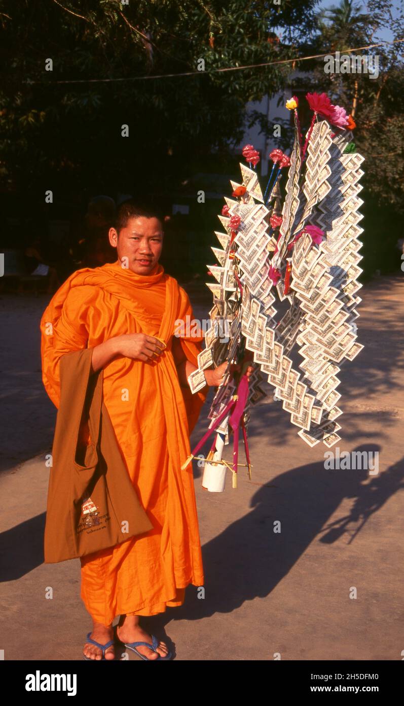 Laos: Un monaco buddista con un 'albero money' (usato per fare il merito), Wat Sainyaphum, Savannakhet, Laos meridionale. In certi momenti del calendario buddista, gli abitanti del villaggio e i laici raccolgono denaro da presentare ai monaci nel loro tempio locale. Questo denaro è vividamente disposto su un 'albero money'. Foto Stock