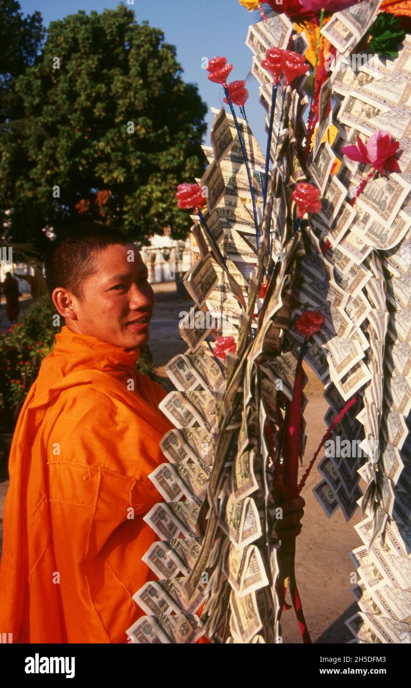 Laos: Un monaco buddista con un 'albero money' (usato per fare il merito), Wat Sainyaphum, Savannakhet, Laos meridionale. In certi momenti del calendario buddista, gli abitanti del villaggio e i laici raccolgono denaro da presentare ai monaci nel loro tempio locale. Questo denaro è vividamente disposto su un 'albero money'. Foto Stock
