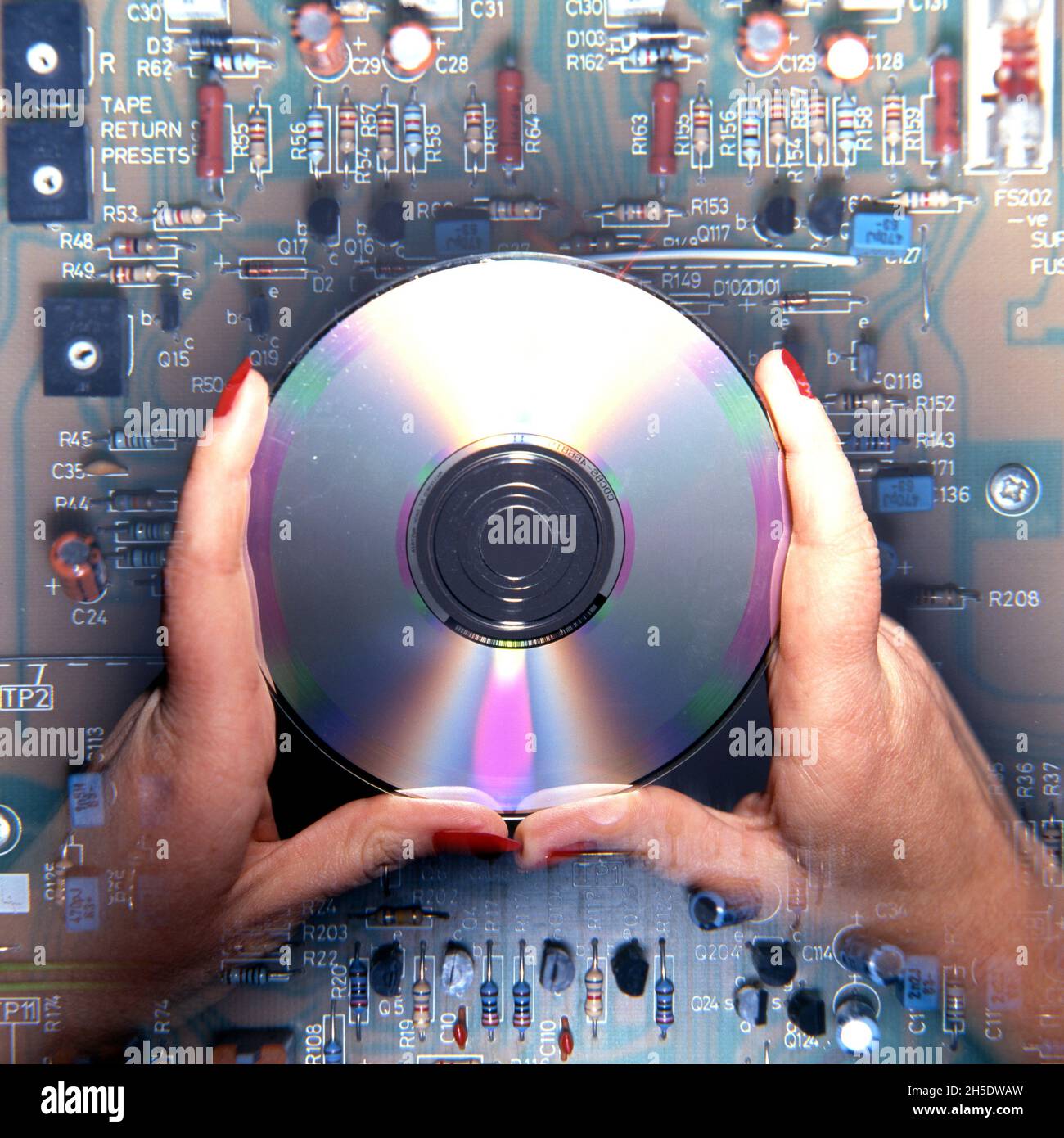 Mani tenendo un CD al di sopra di un circuito elettronico, Regno Unito, Europa occidentale. Foto Stock