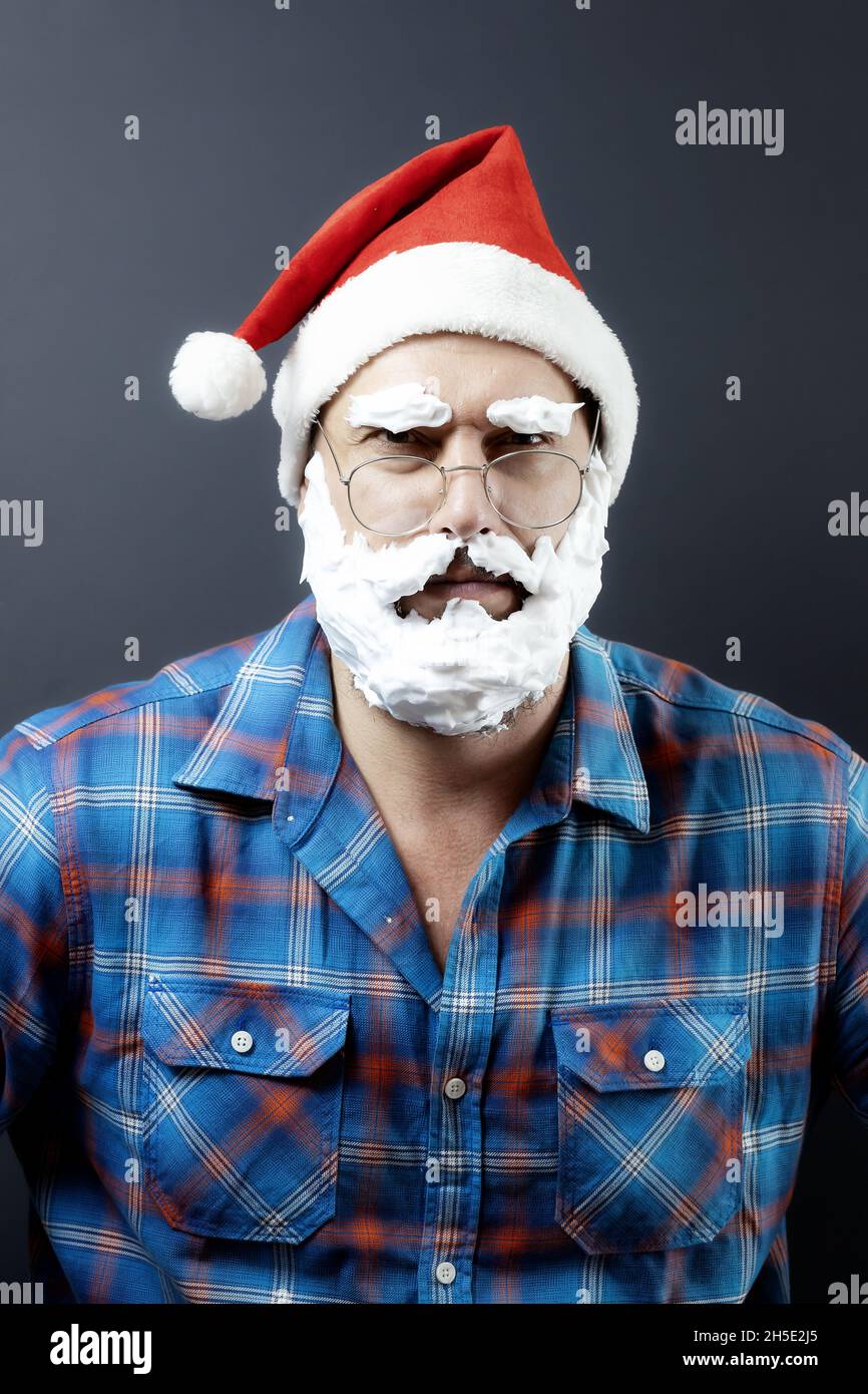 Un uomo in un cappello di santa con una barba bianca da neve finta e baffi  che accovacciano le sopracciglia bianche sembra piercing Foto stock - Alamy